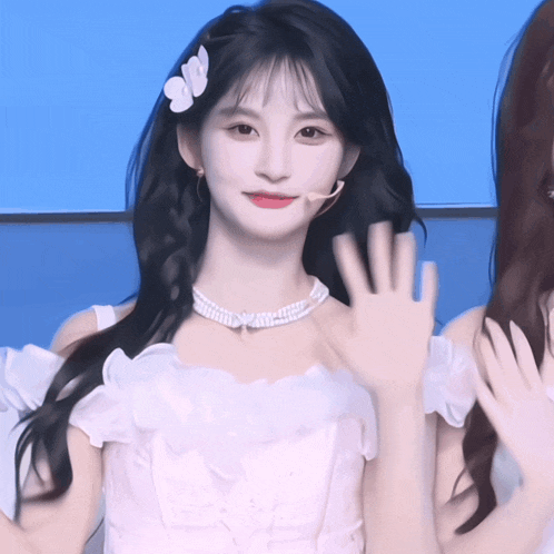 a woman in a white dress with a flower in her hair waves
