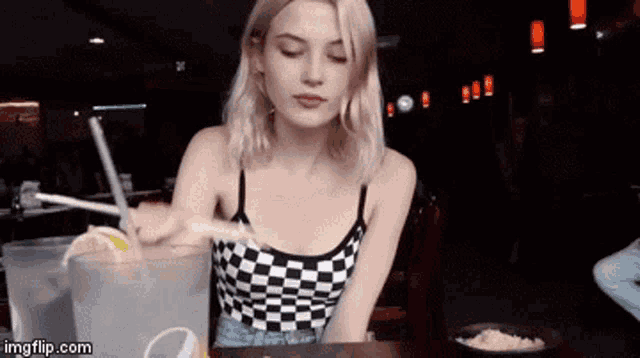 a woman in a checkered tank top is sitting at a table with a pitcher of water and a lemon slice .