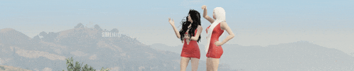 two women in red dresses are standing in front of a mountain with the hollywood sign in the background