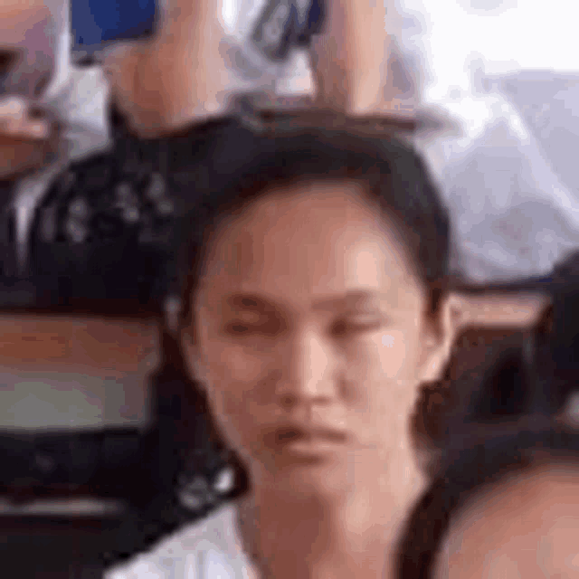 a woman is sitting in a classroom with her eyes closed and a group of people behind her .