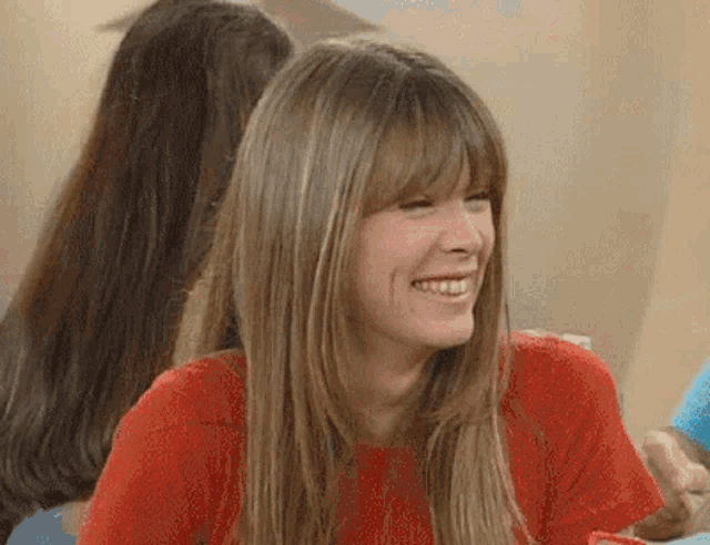 a woman with long blonde hair and bangs is smiling while sitting at a table .