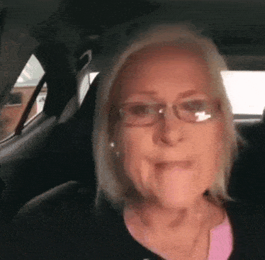 a woman wearing glasses is sitting in the back seat of a car and making a funny face .