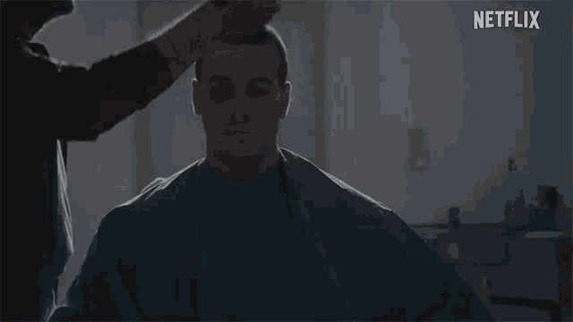 a man is getting his hair cut in a dark room with a netflix logo in the corner .