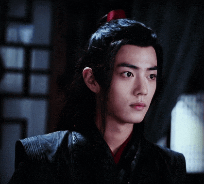 a young man with long black hair and a red ponytail is looking at the camera .