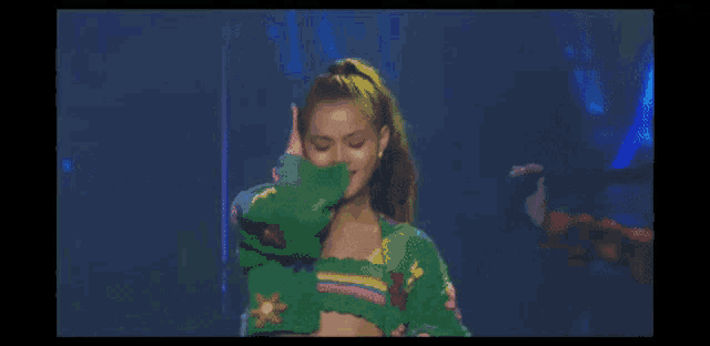 a woman wearing a green sweater with flowers on it is dancing on a stage