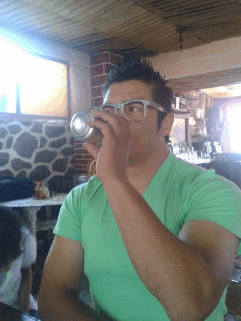 a man in a green shirt drinks from a can