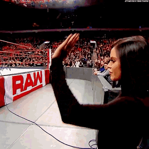 a woman stands in front of a raw sign in a wrestling ring .
