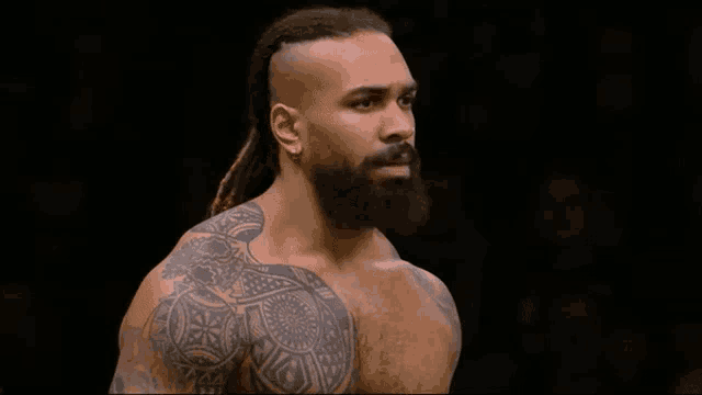 a man with dreadlocks and a beard has a tattoo on his shoulder