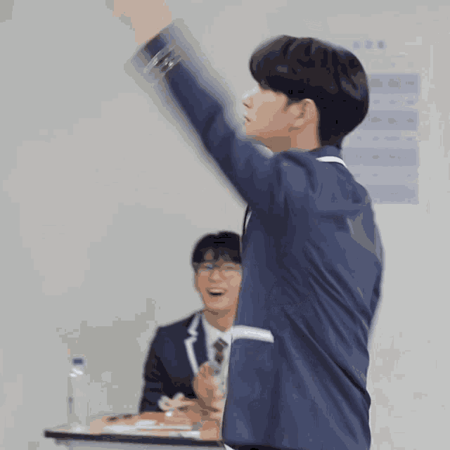 a man in a suit and tie is standing in front of a table with his arms in the air