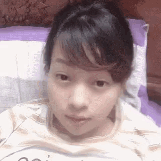 a woman is laying on a bed with a purple pillow behind her
