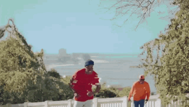 two men in orange shirts are standing next to each other on a hill .