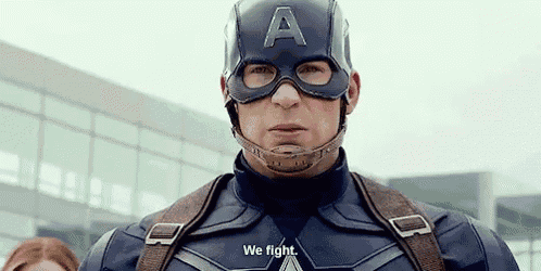captain america is wearing a helmet and goggles and says `` we fight '' while standing in front of a building .