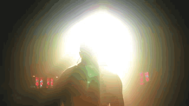 a man is standing in a dark room with a light behind him and a clock that says 10:16