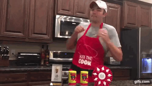 a man wearing a red apron that says kiss the cook on it