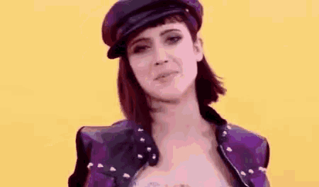 a woman wearing a hat and a purple jacket is making a face .
