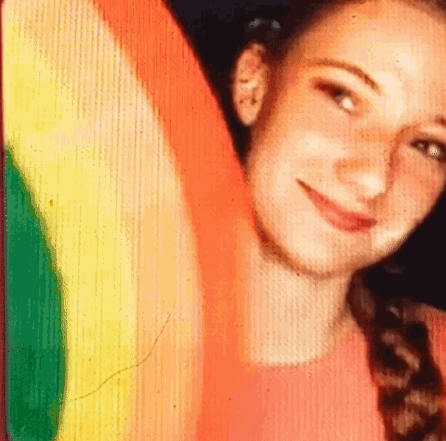 a girl is smiling in front of a rainbow colored background
