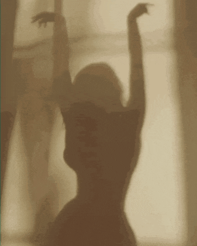a shadow of a woman dancing in front of a window with her arms in the air .
