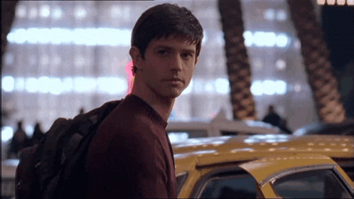 a man with a backpack stands in front of a yellow taxi cab