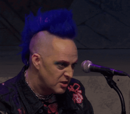 a man with blue hair singing into a microphone