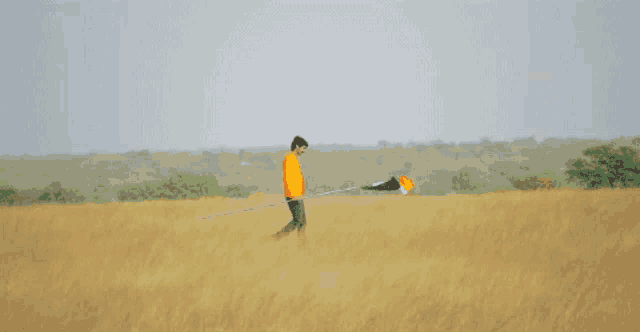 a man in an orange shirt is walking in a field holding a flag