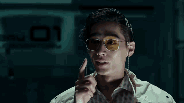 a man wearing sunglasses and a white jacket has the number 01 on the wall behind him