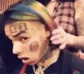 a man with a tattoo on his face is being shaved by a man .