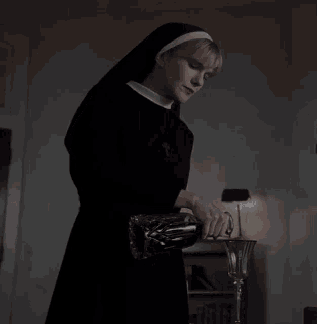 a nun in a black robe holds a glass bottle