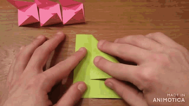 a person folding a piece of green paper with the words made in animotica visible