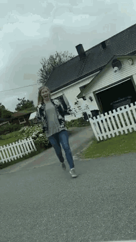 a woman is walking down a street in front of a house