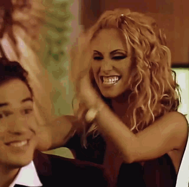a woman with curly hair is smiling and holding a man 's hair