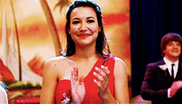 a woman in a red dress is clapping her hands in front of a man in a suit