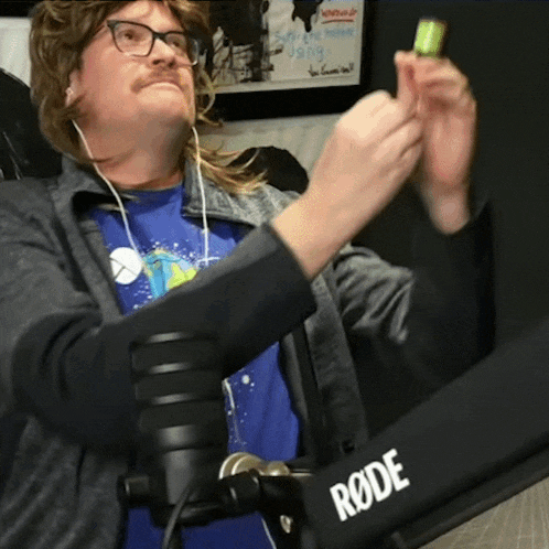 a man in a blue shirt is standing in front of a rode brand microphone