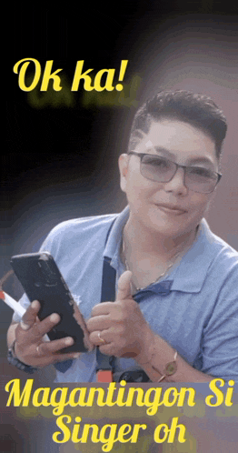 a man with glasses is holding a cell phone and giving a thumbs up sign