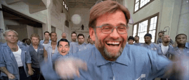 a man with glasses and a beard is smiling in front of a group of prisoners