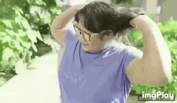 a woman wearing glasses and a blue shirt is holding her hair .