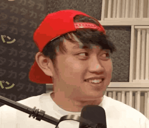 a young man wearing a red hat and a white shirt is smiling in front of a microphone .