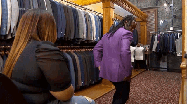 a man in a purple jacket is standing in front of a woman in a suit store