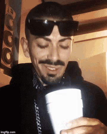a man wearing sunglasses and a bandana holds a styrofoam cup