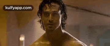 a shirtless man with long hair is standing in a room and smiling at the camera .