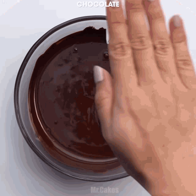 a close up of a person 's hand reaching into a bowl of chocolate
