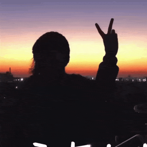 a silhouette of a person giving the peace sign at sunset