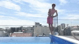 a man in pink shorts is standing on the edge of a pool .
