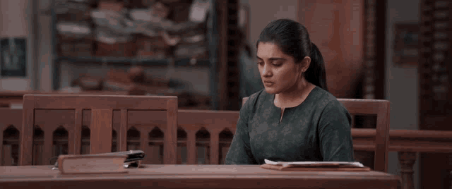 a woman in a green shirt sits at a wooden table