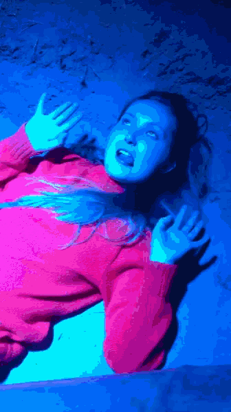 a woman in a pink sweater is laying on the floor in a dark room