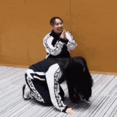 two women are kneeling on the floor and one is sitting on the other 's lap .