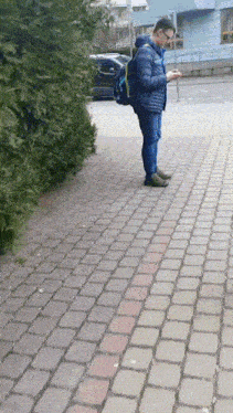 a man with a backpack standing on a sidewalk looking at his phone