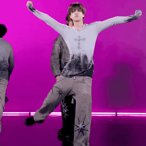 a man in a tie dye shirt with a cross on it is dancing on a purple background .