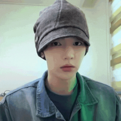 a man wearing a hat and a denim jacket looks at the camera .
