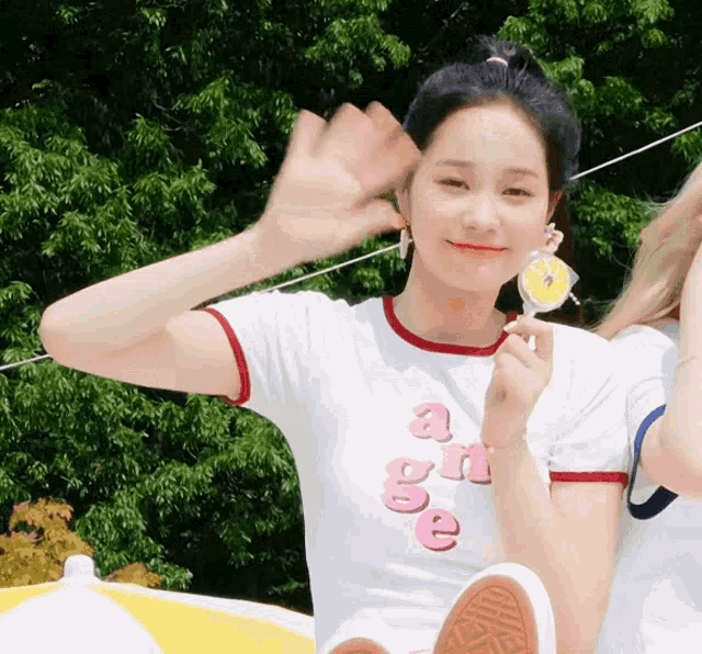 a girl wearing a white shirt with the word age on it holds a lollipop