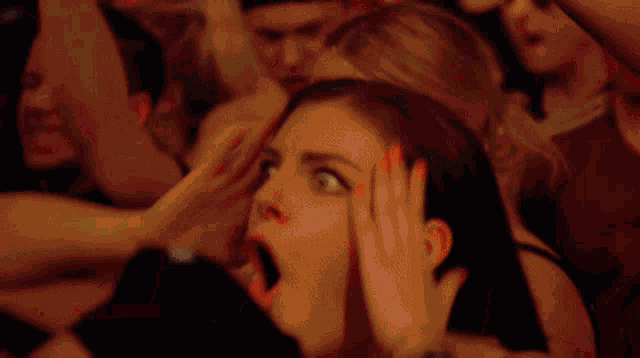 a woman with her mouth open holds her hands to her head